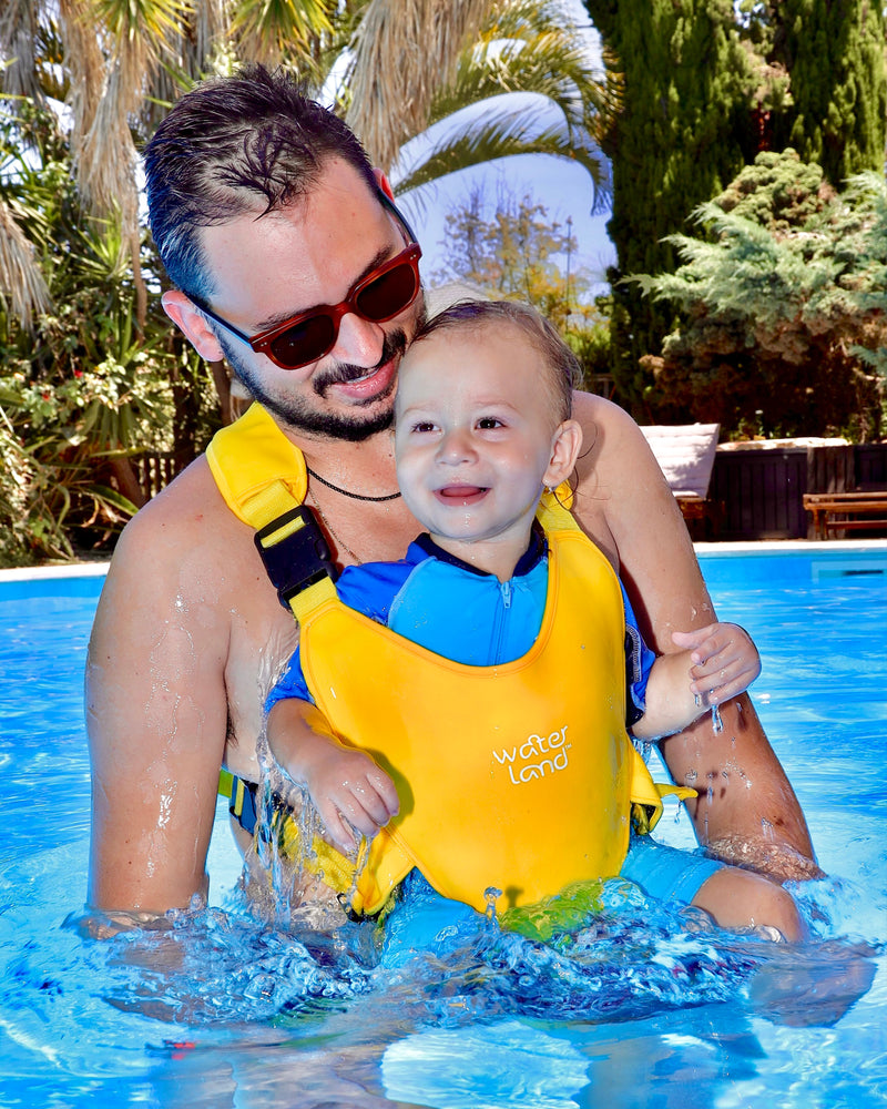 A baby in a Yellow Sunrise WaterLand carrier in a garden pool, water splashing